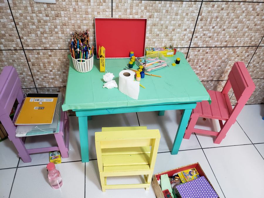 Mesa infantil com lápis de cor, tintas e cadeiras coloridas