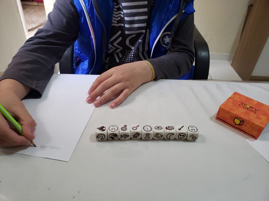 Criança escrevendo durante uma sessão, com dados de contar histórias sobre a mesa